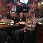 A group of people sitting at a table holding up a check.