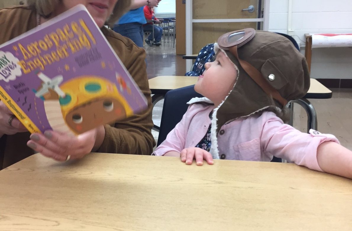 A woman reading to a child at the table.