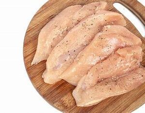 Raw chicken breasts on cutting board.