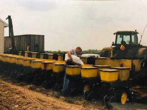 A man standing next to a row of yellow seed planters.