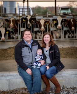 A man, woman and baby sitting in front of cows.