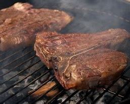 Two T-bone steaks grilling on a barbecue.