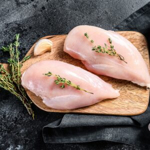 Two raw chicken breasts on a cutting board.