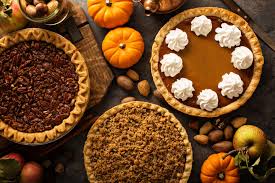 A table topped with pies and pumpkins next to nuts.