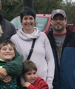 A family posing for a picture in front of some cars.