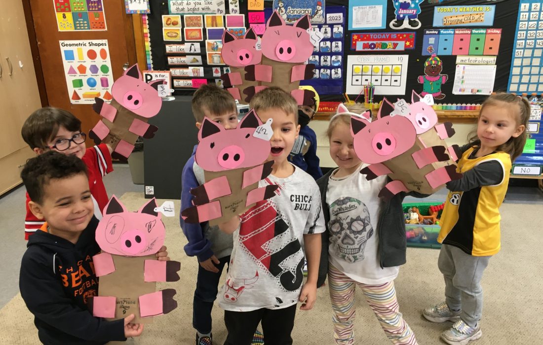 A group of children holding up paper pigs.