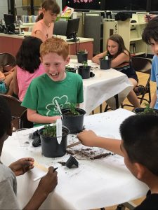 A group of children sitting around a table with plants.