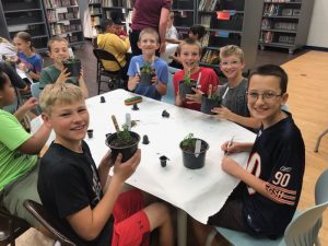 A group of kids sitting around a table with plants.