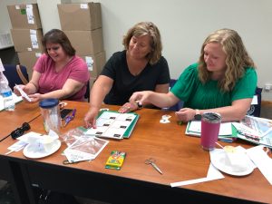 Three women sitting at a table with paper and pencils.