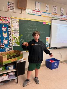 A boy in front of a chalkboard holding a stick.