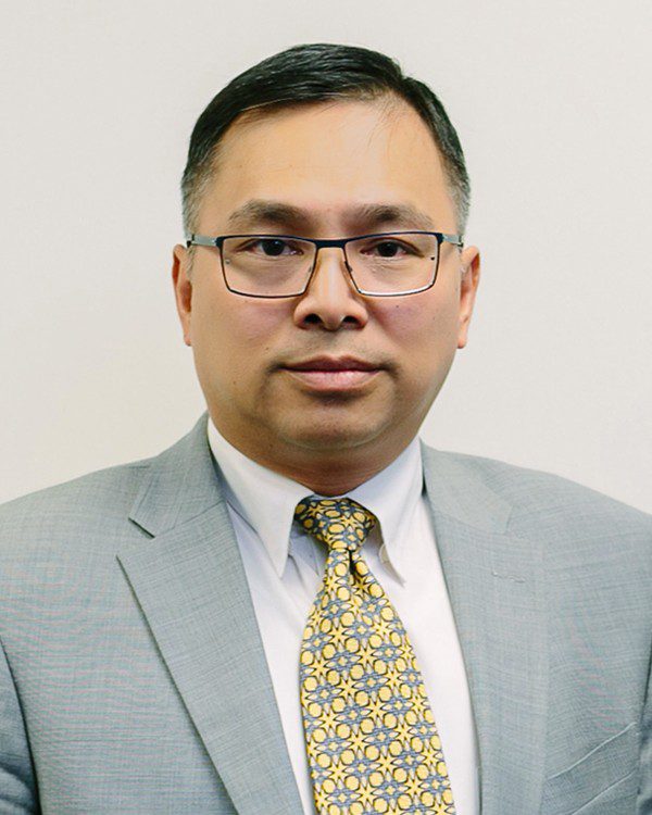 Man in suit and glasses, neutral background.